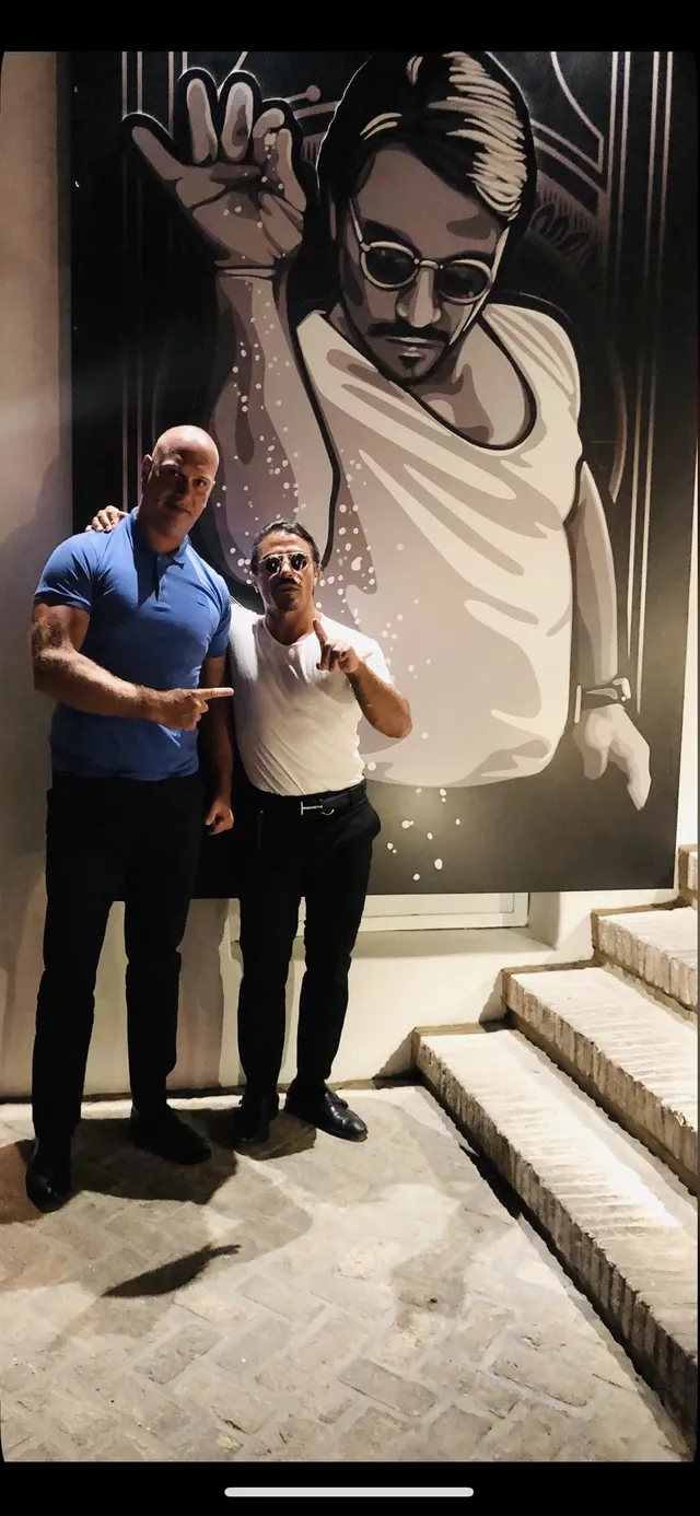 Two men posing beside a chef mural at a restaurant